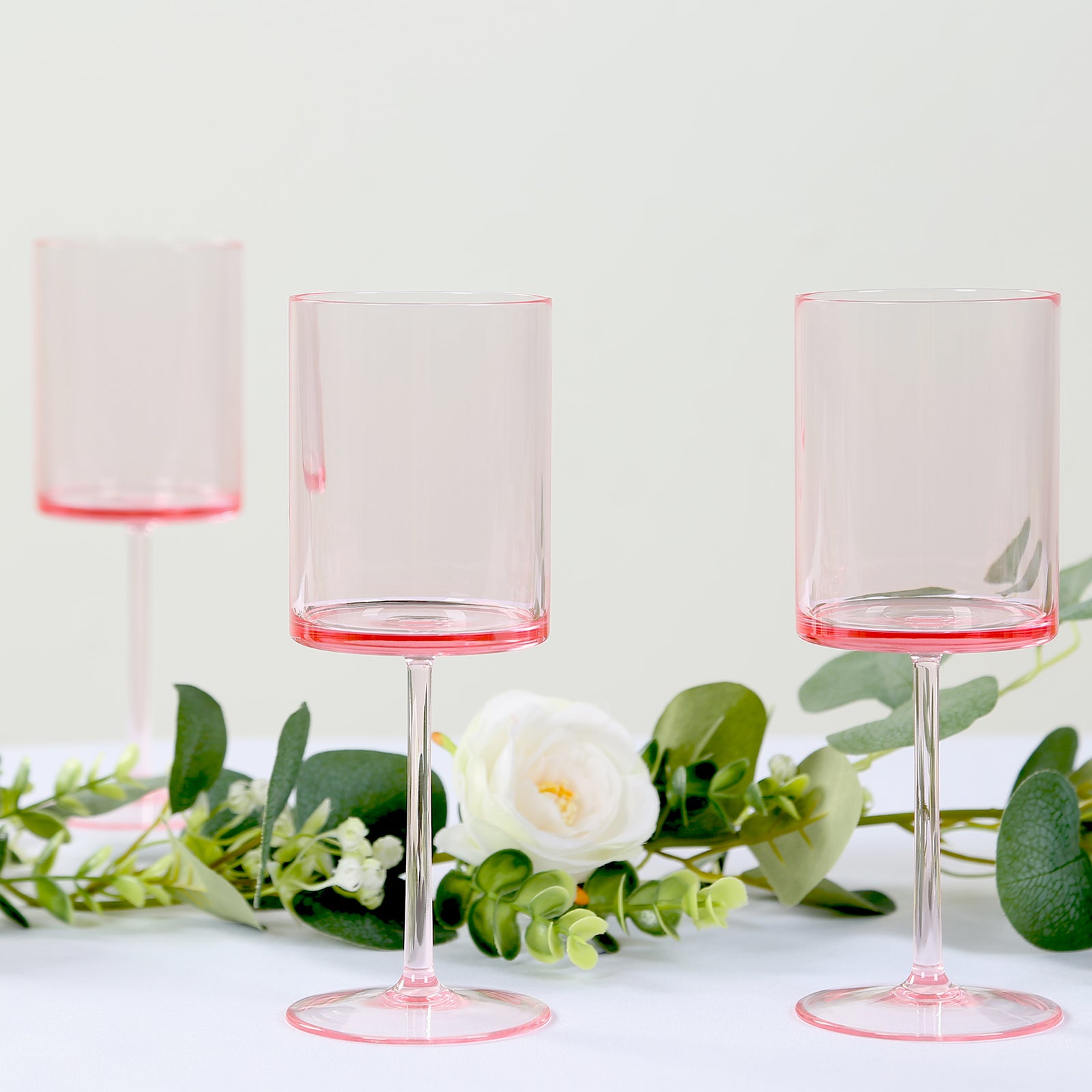 Transparent blush plastic reusable cocktail glasses with long stems.