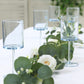 Transparent dusty blue cocktail glasses with long stems on a table.