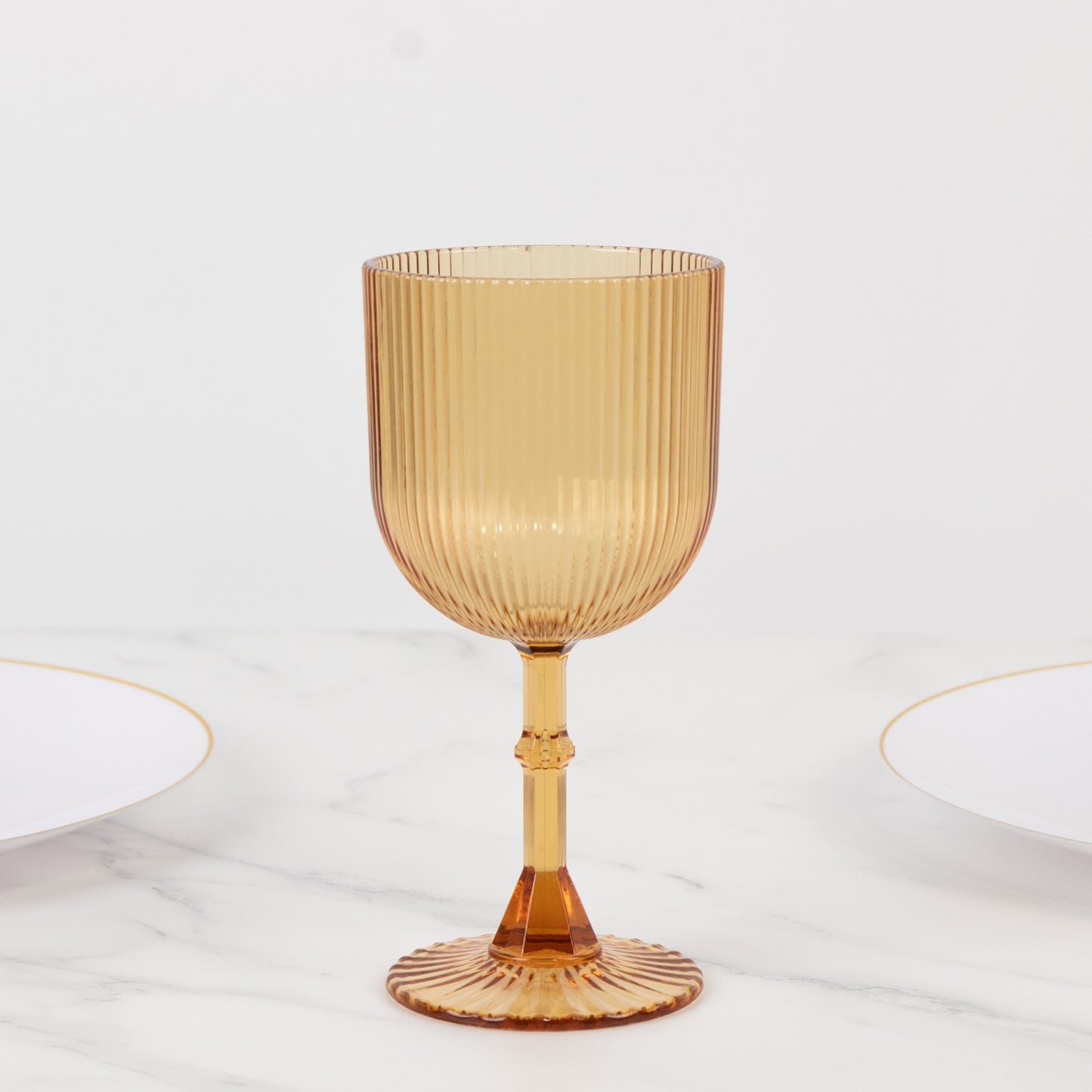 Amber gold ribbed reusable plastic wine goblet on a marble surface.