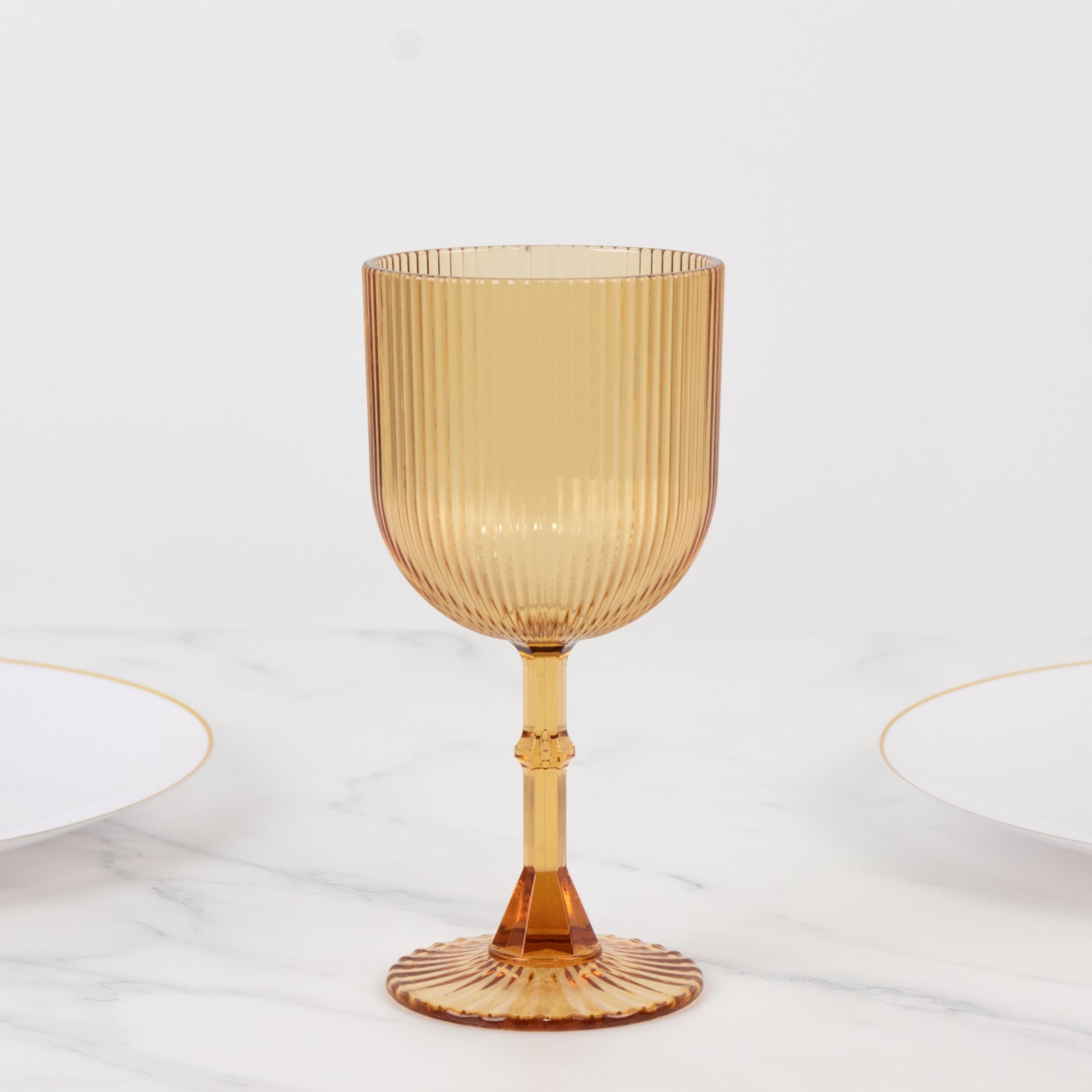 Amber gold ribbed reusable plastic wine goblet on a marble surface.