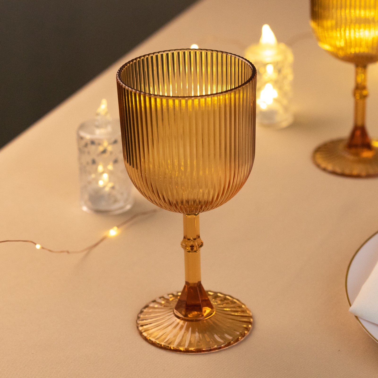 Amber gold ribbed reusable plastic wine goblet on a table setting.
