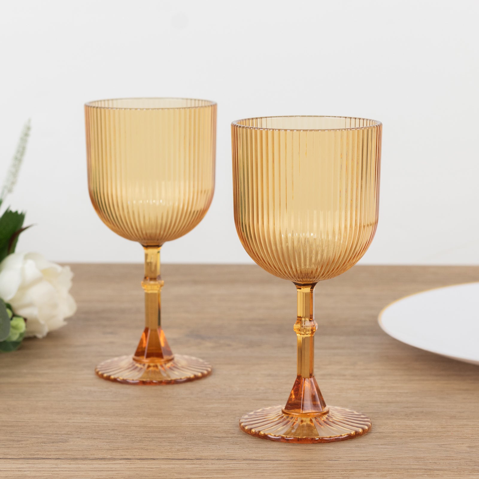 Amber gold ribbed reusable plastic wine goblets on a wooden table.