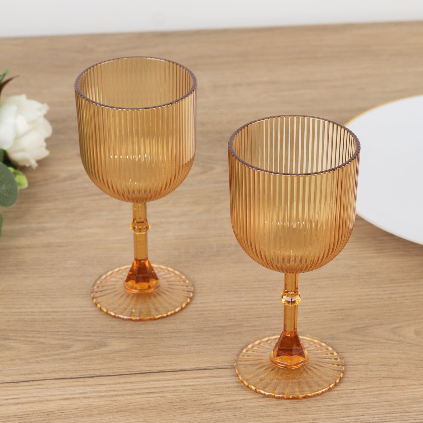 Amber gold ribbed reusable plastic wine goblets on a wooden table.