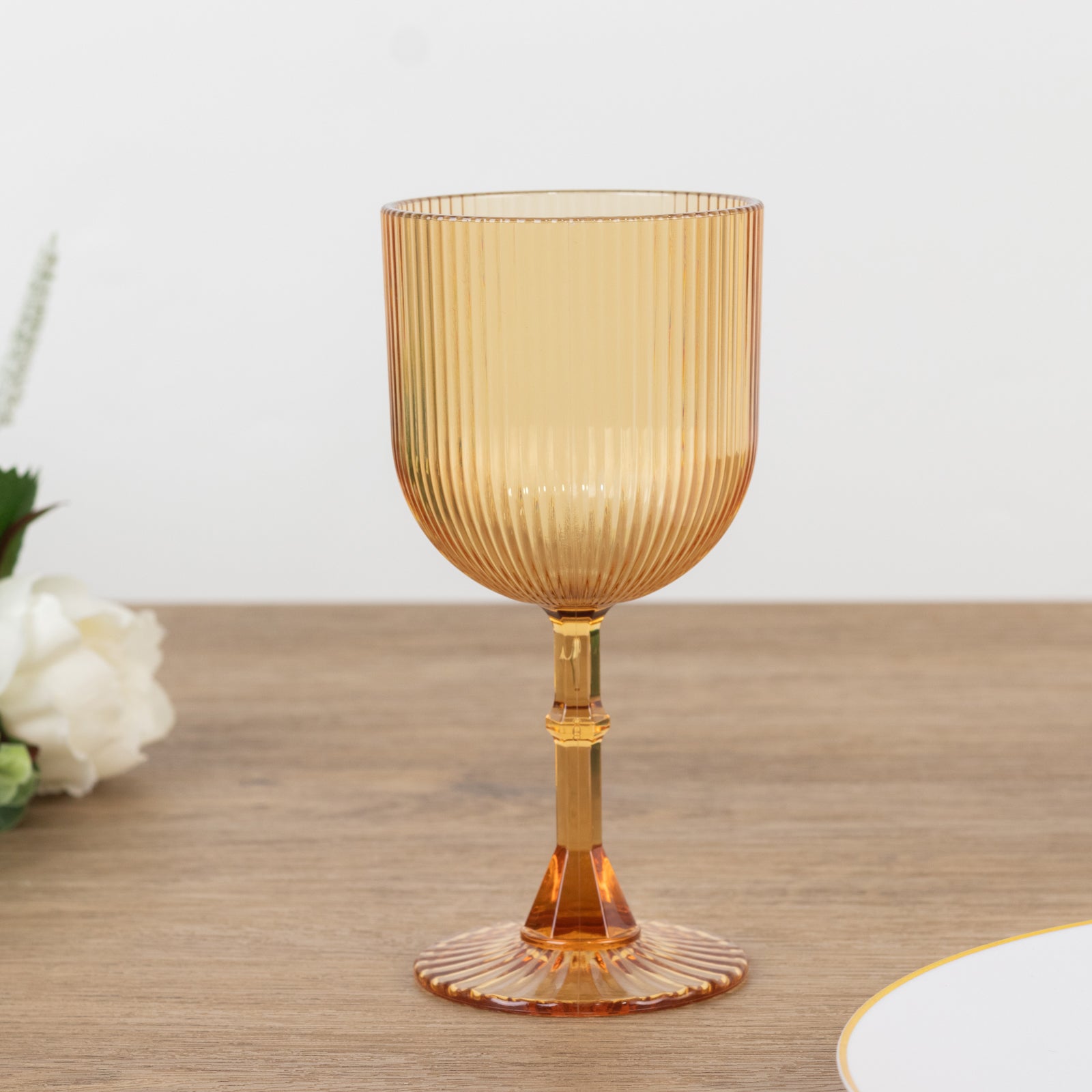 Amber gold ribbed reusable plastic wine goblet on a wooden surface.