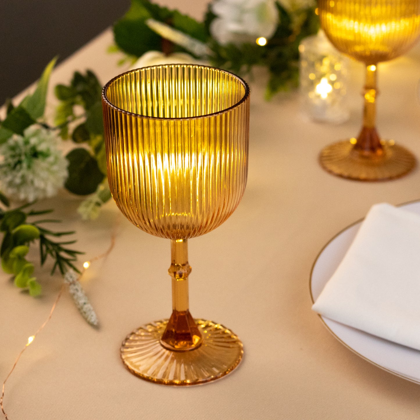 Amber gold ribbed reusable plastic wine goblet on a table setting.