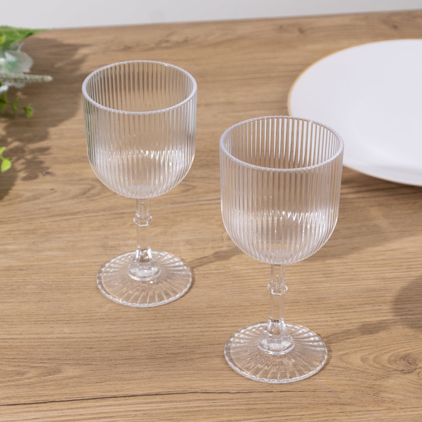 Clear ribbed reusable plastic wine goblets on a wooden table.