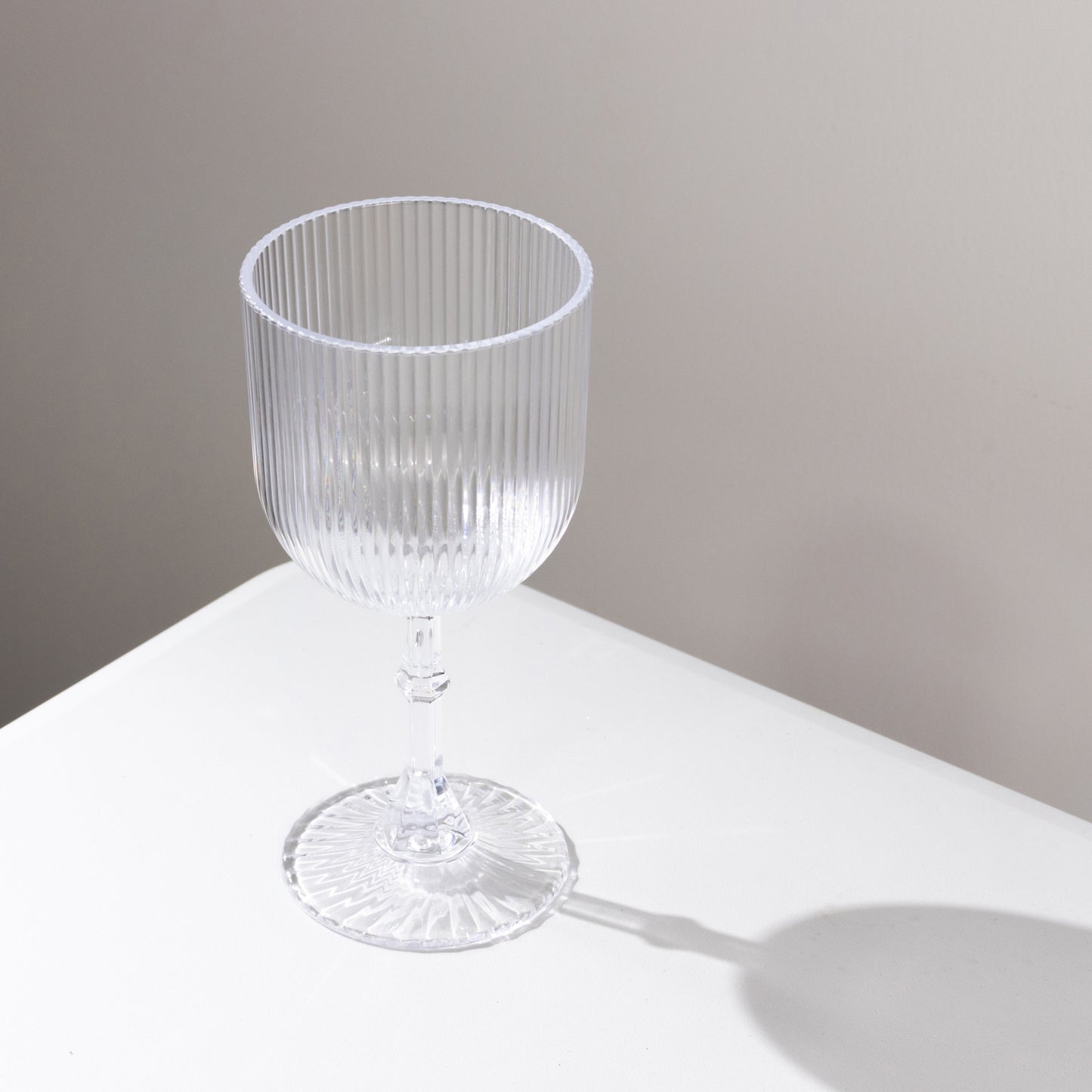 Clear ribbed shatterproof wine goblet on a white surface.