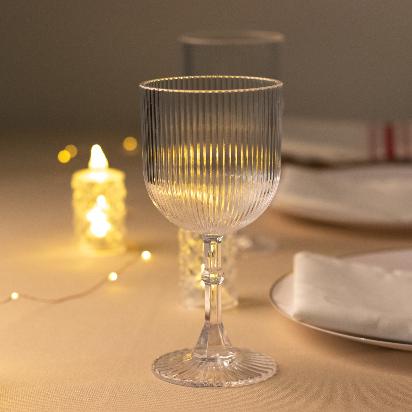 Clear ribbed shatterproof wine goblet on a table with warm lighting.
