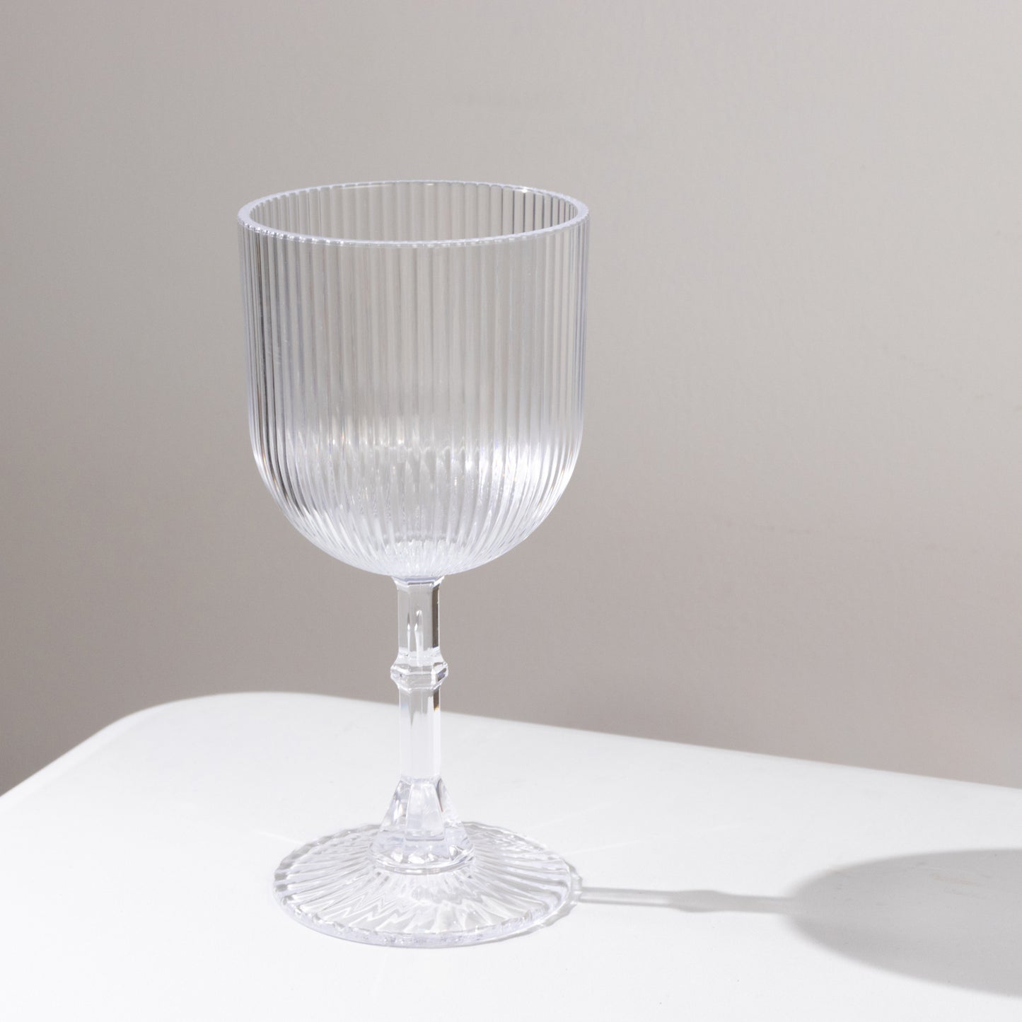 Clear ribbed shatterproof wine goblet on a white surface.