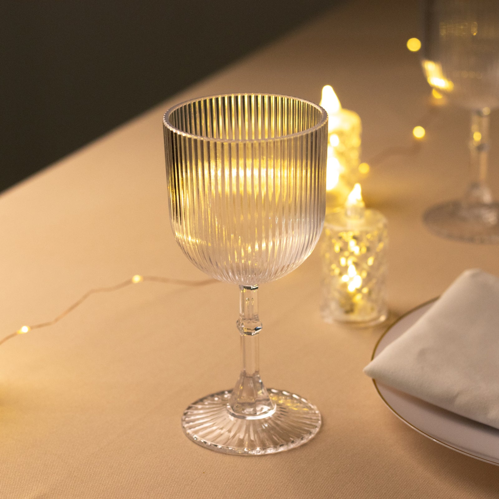 Clear ribbed reusable plastic wine goblet on a table with soft lighting.