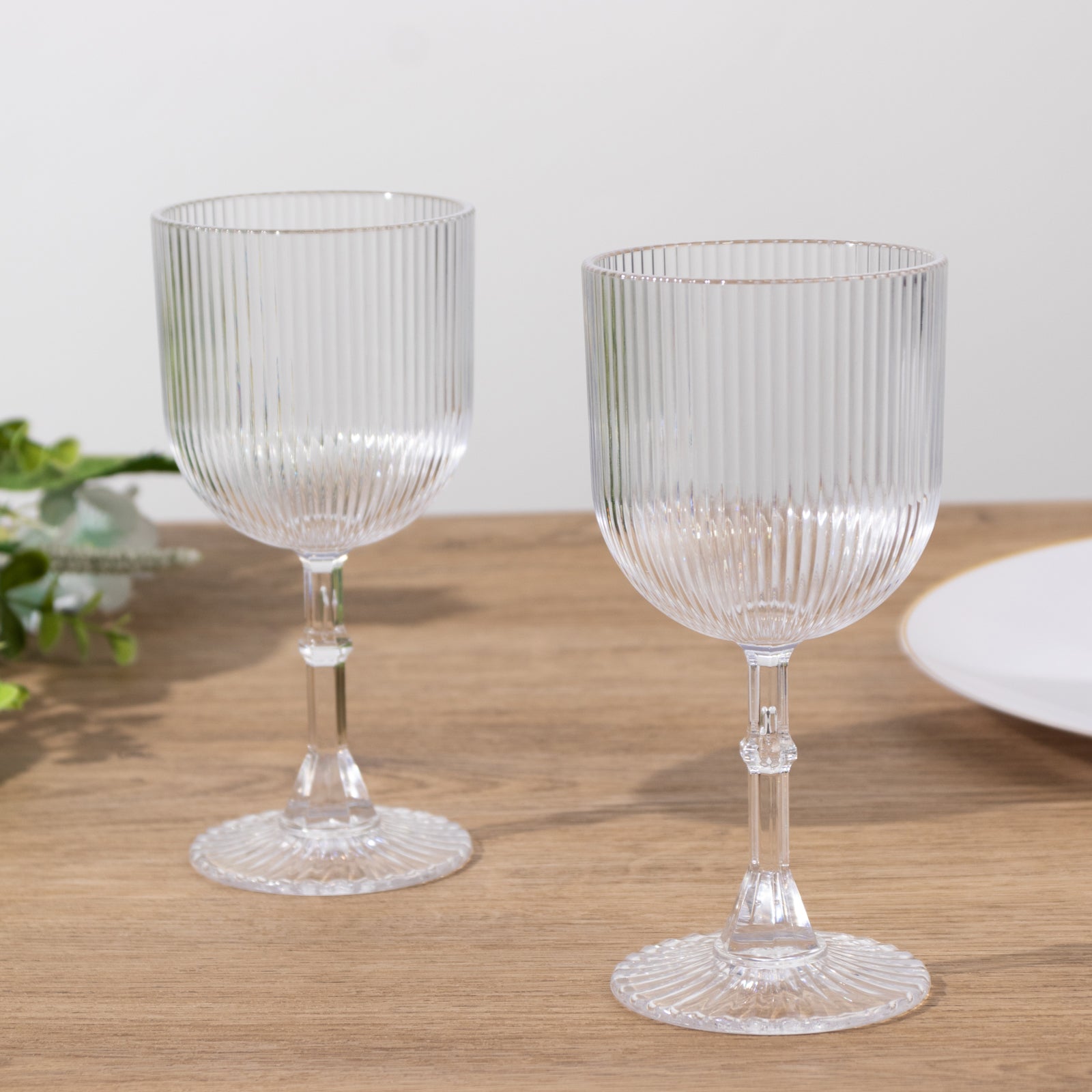 Clear ribbed reusable plastic wine goblets on a wooden table.