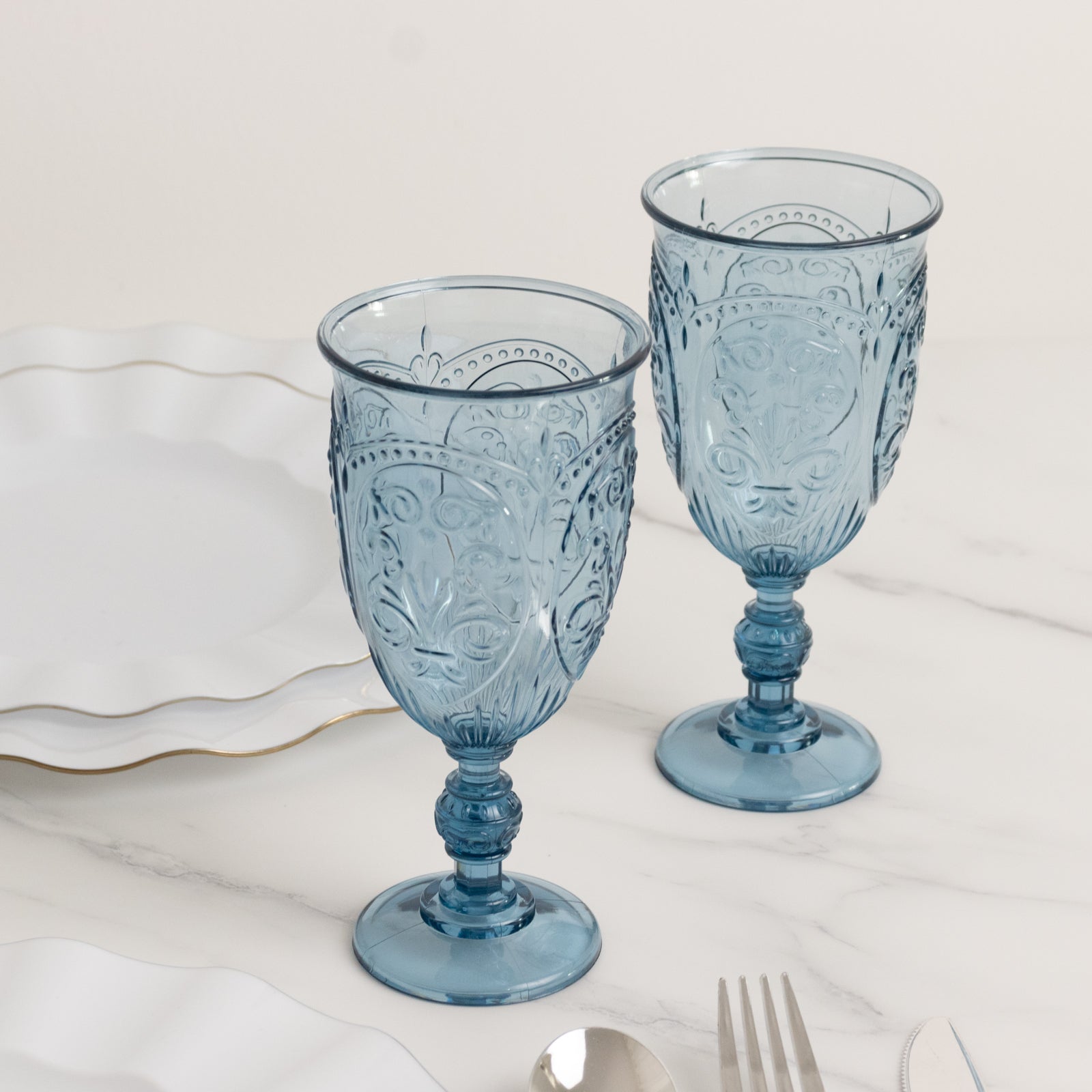 Transparent dusty blue vintage goblets with embossed design on marble table.