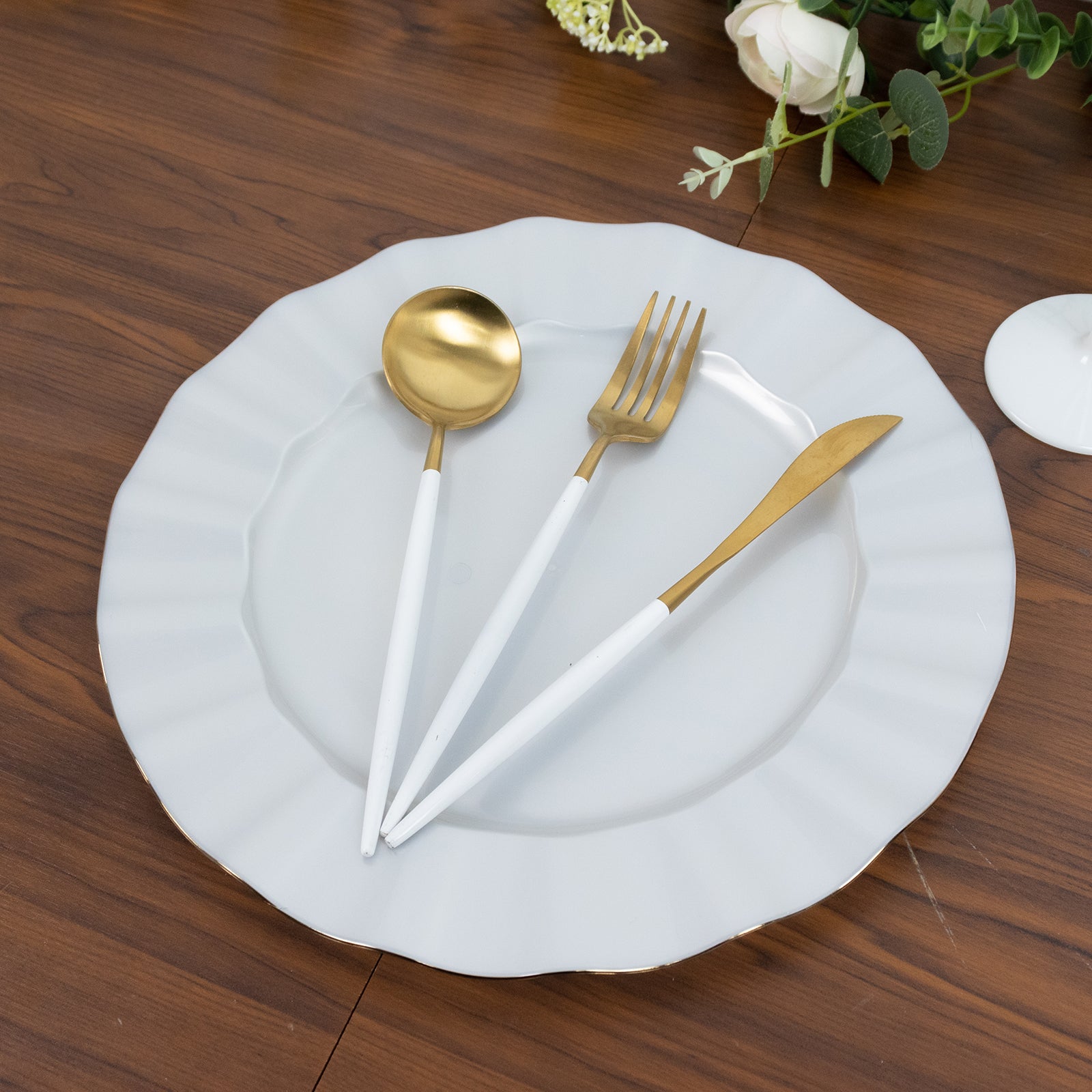 Pearl white round dinner plate with gold edging and elegant utensils on a wooden table.