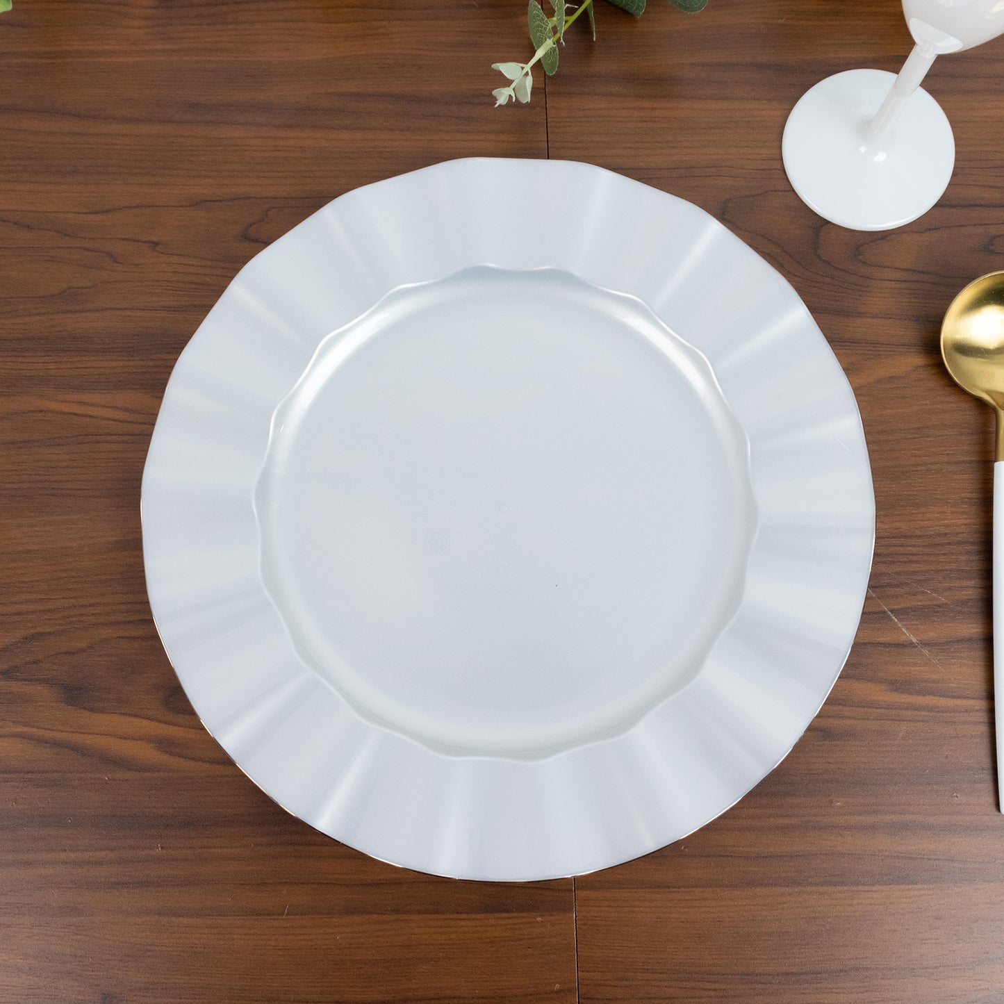 Pearl white ruffled rim dinner plate with gold edging on a wooden table.