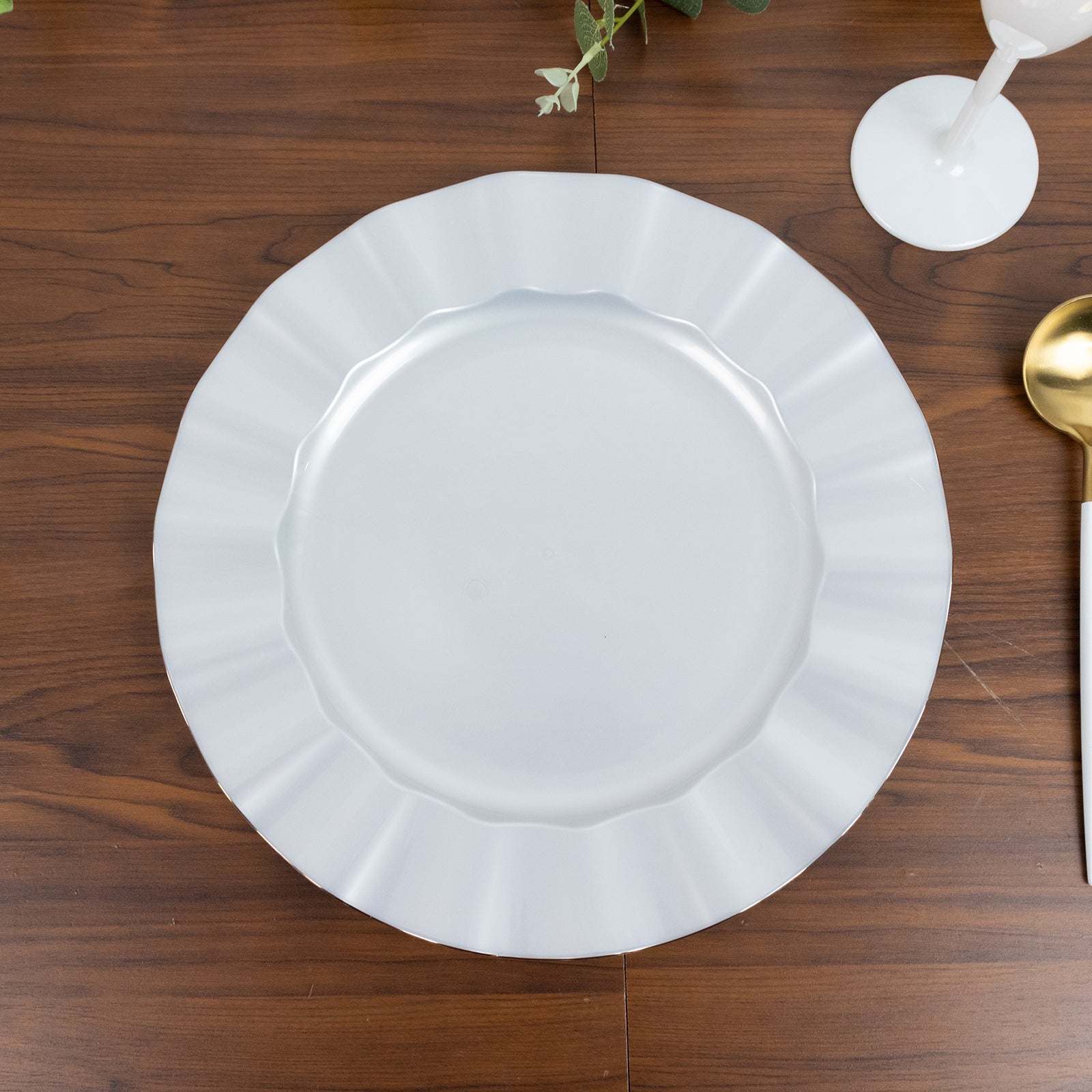 Pearl white ruffled rim dinner plate with gold edging on a wooden table.