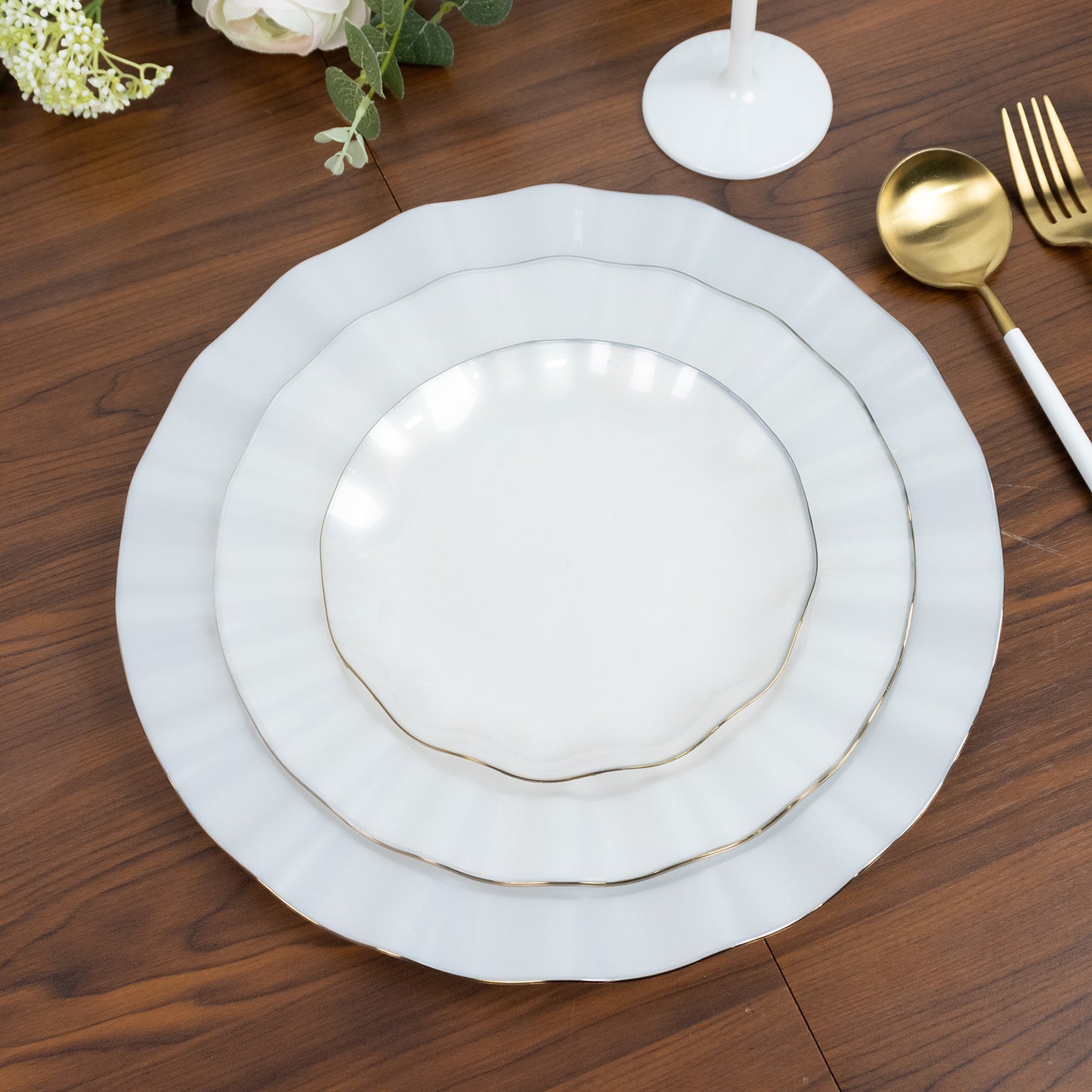 Pearl white round dessert plates with gold edging, set on a wooden table.