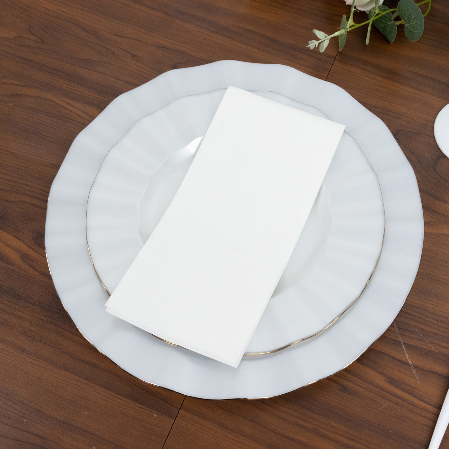 Pearl white ruffled rim dinner plate with gold edging on a wooden table.