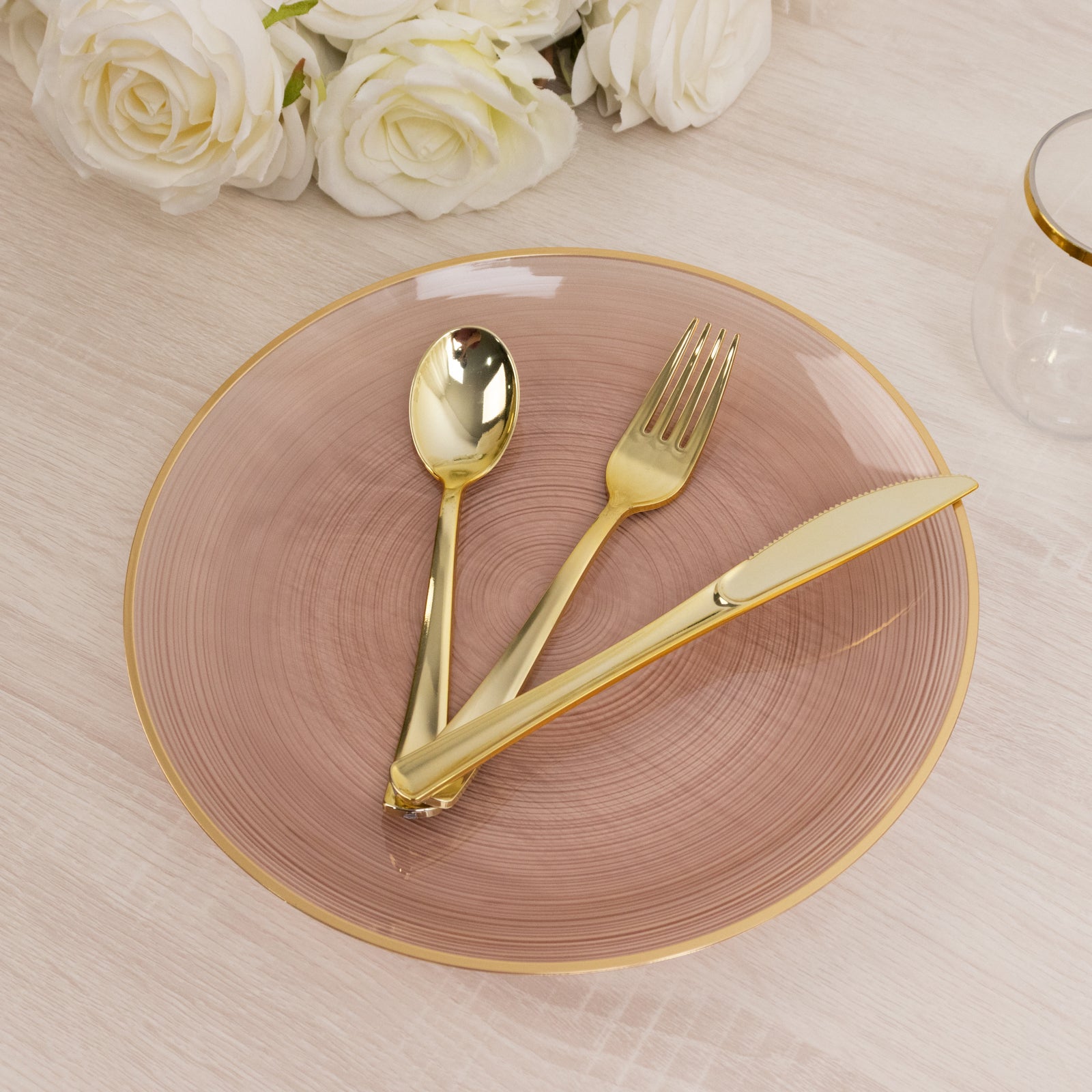 Dusty rose swirl plastic dinner plate with gold rim and cutlery on a table.