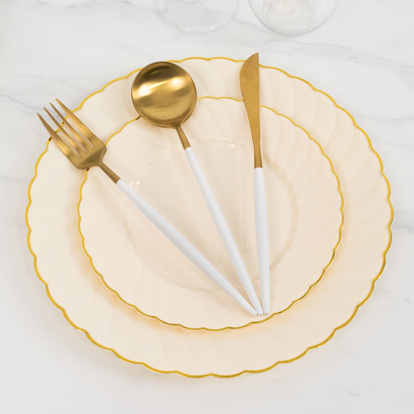 Ivory and gold flair rim disposable dessert plates stacked on a marble surface.