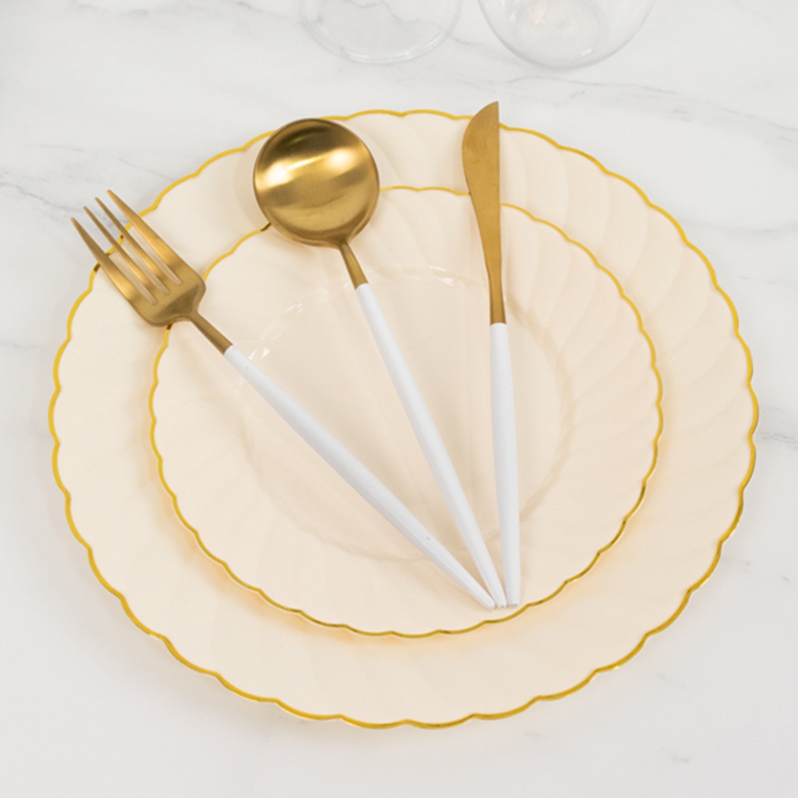 Ivory and gold flair rim disposable dessert plates stacked on a marble surface.