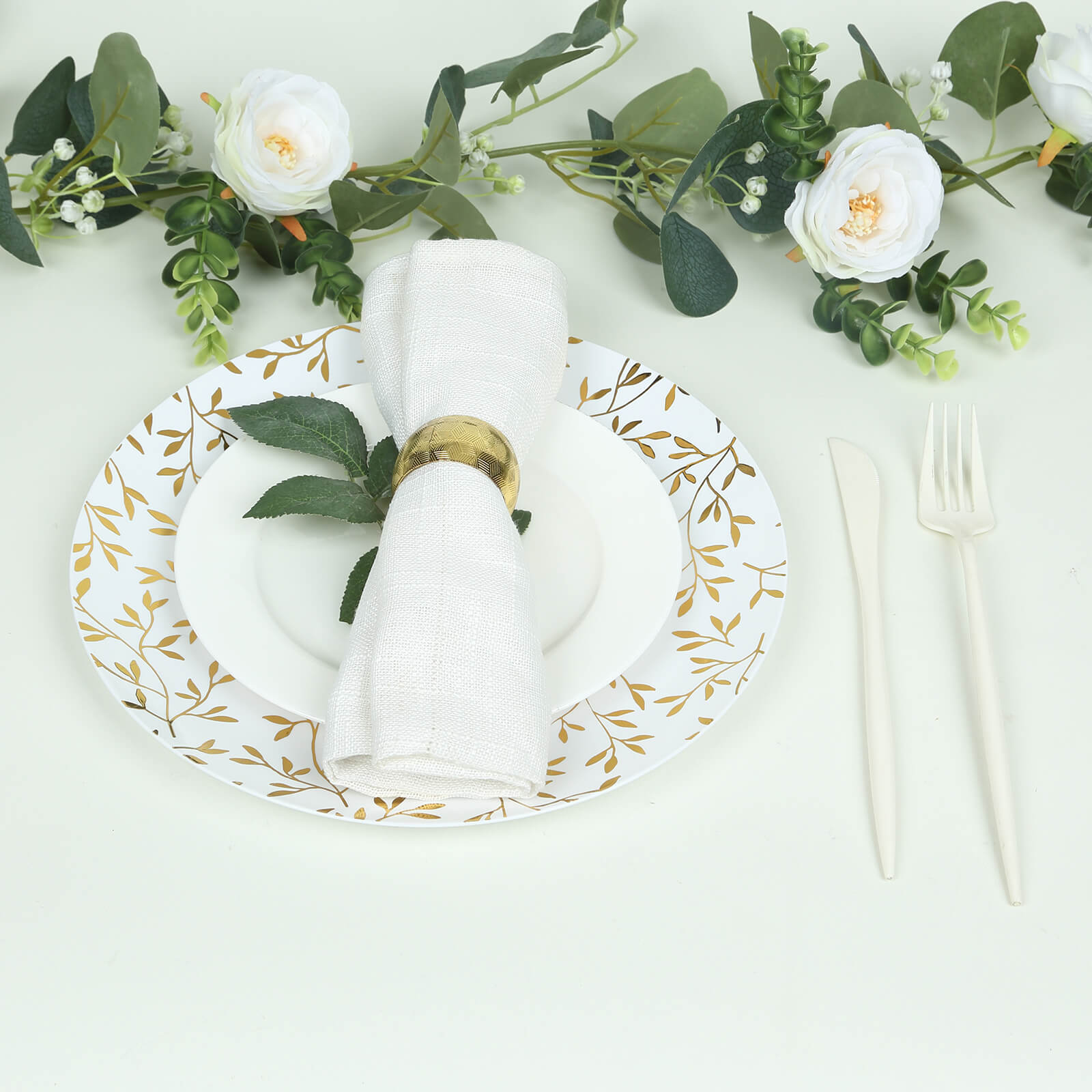 White round plastic party plates with gold leaf design on a table setting.