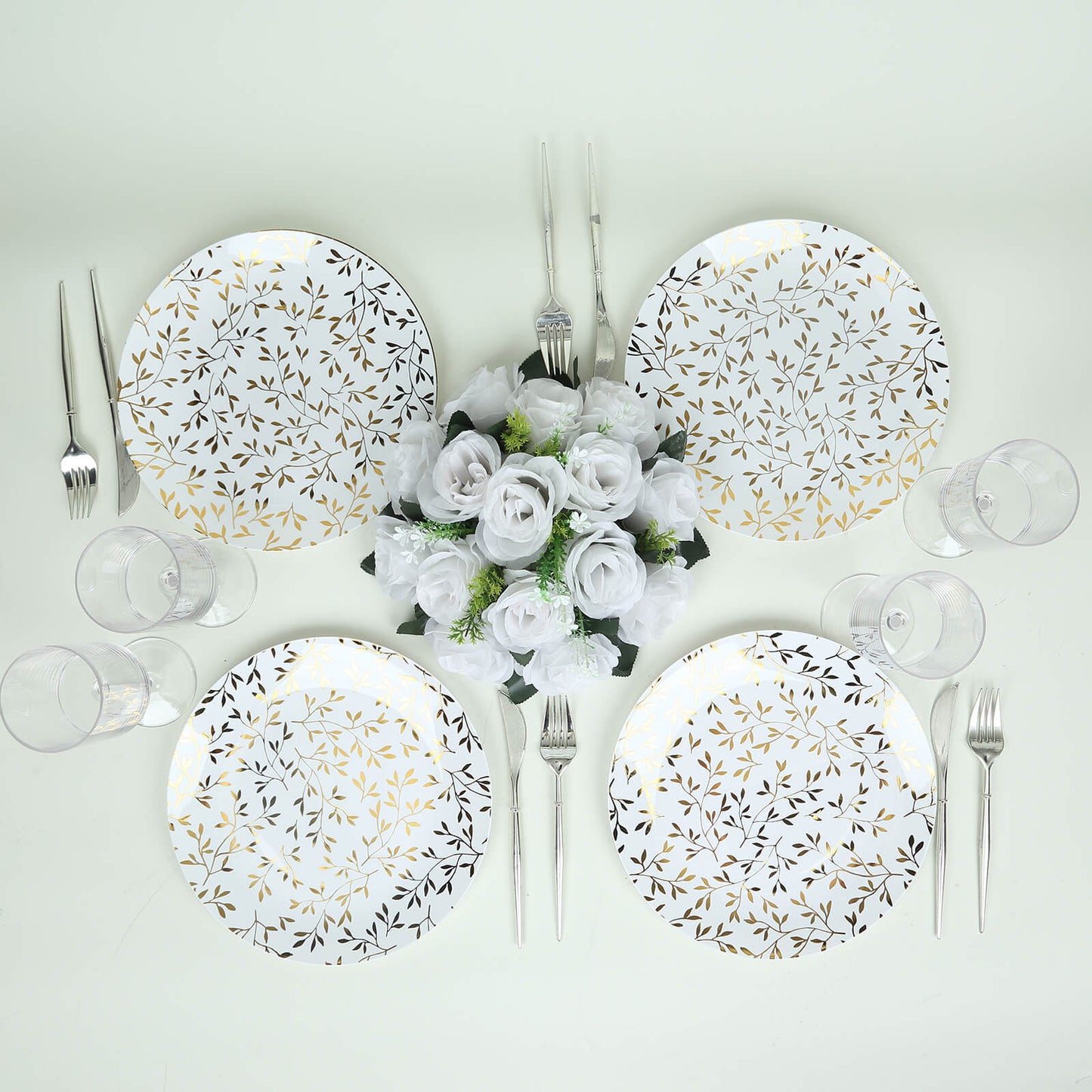 White round plastic party plates with gold leaf design on a table setting.