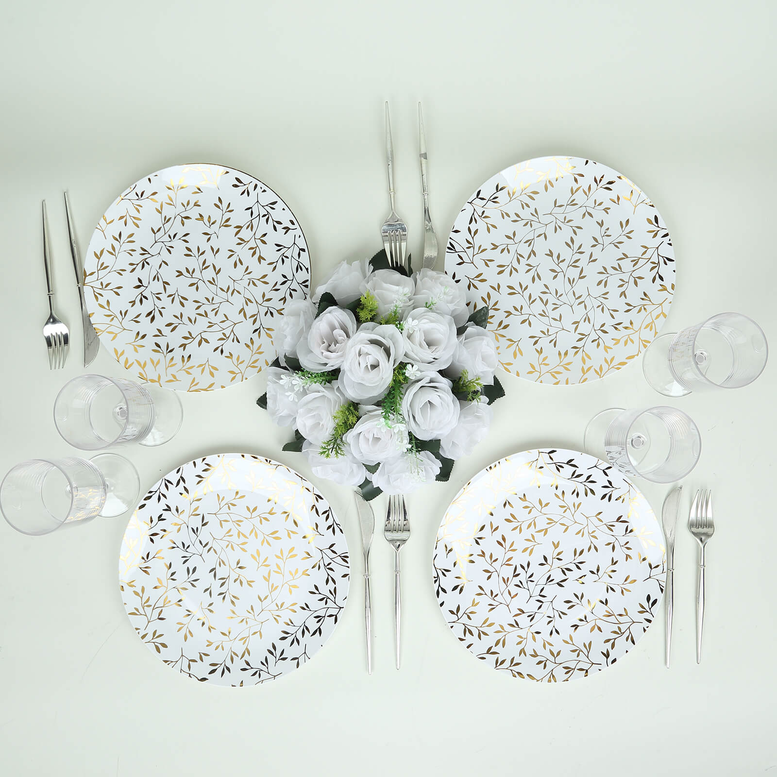 White round plastic party plates with gold leaf design on a table setting.