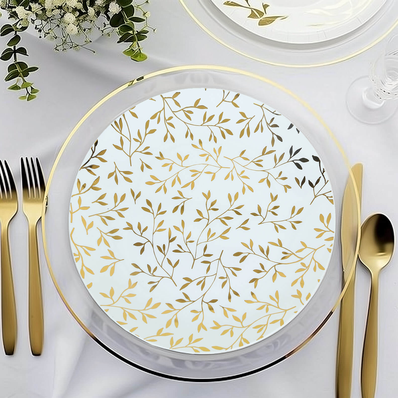 White round plastic party plate with gold leaf design on a table setting.