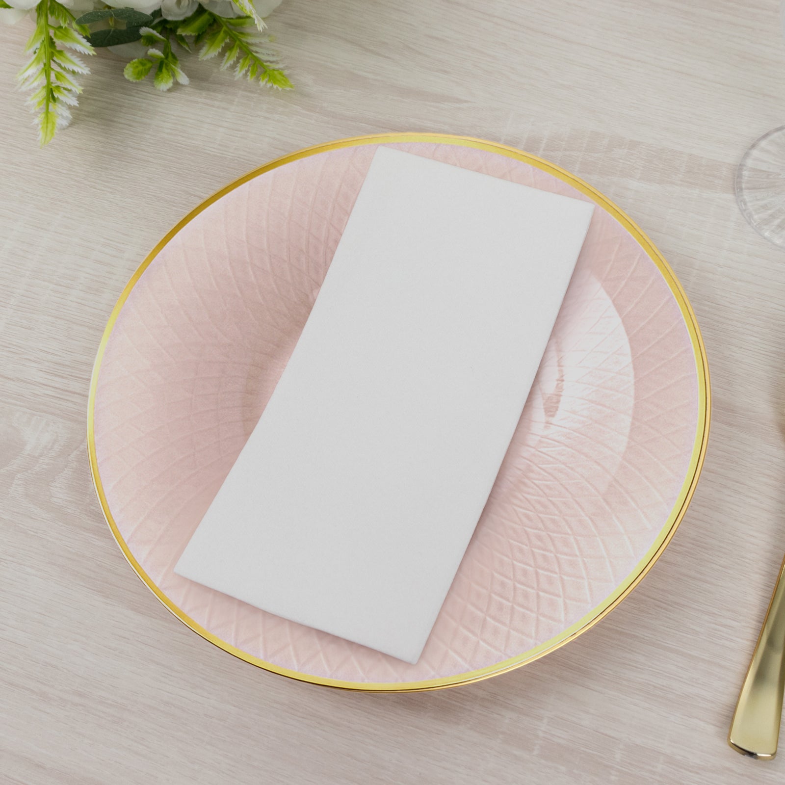 Blush pink round plastic dinner plate with gold rim and diamond-cut pattern.