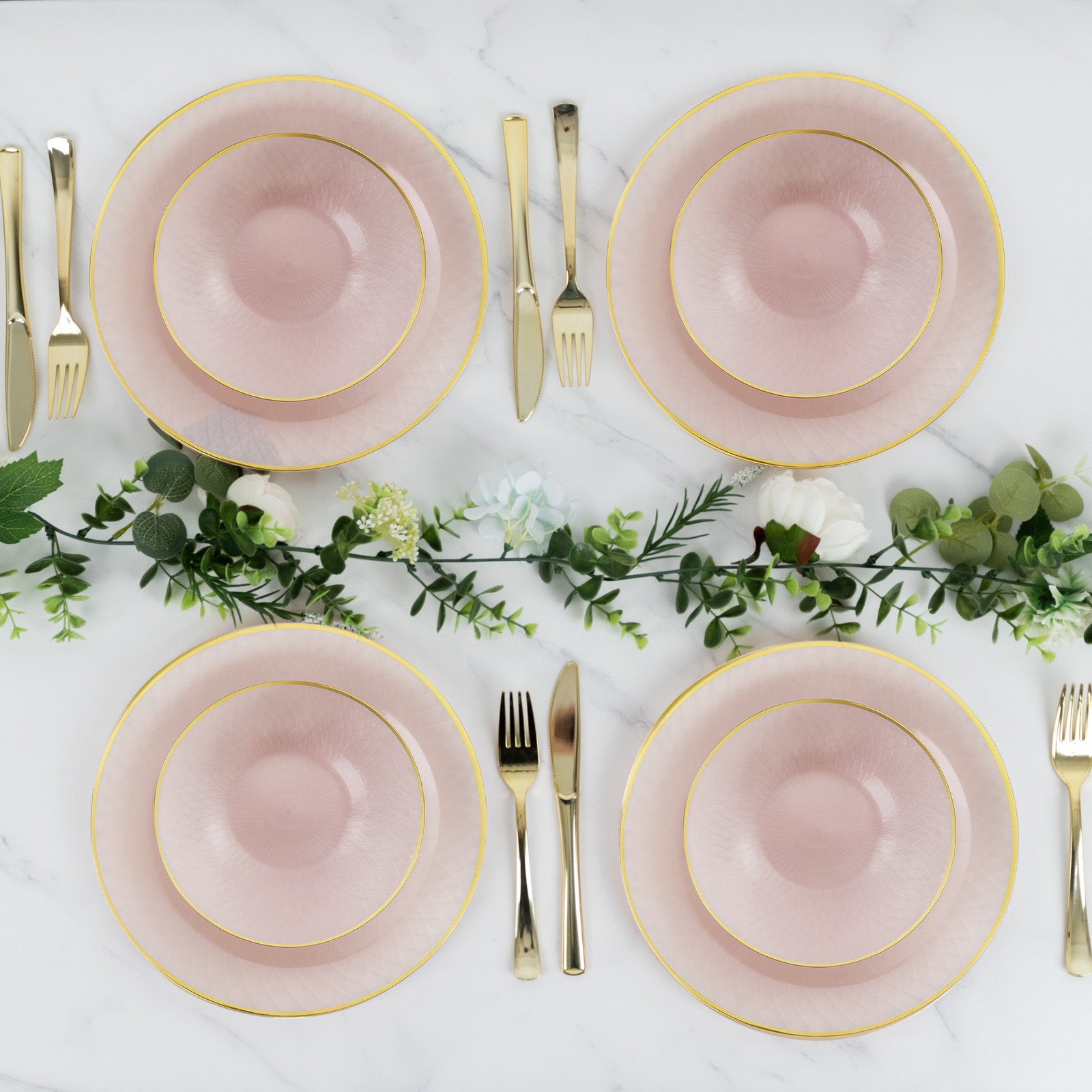 Blush pink round dessert plates with gold rims on a marble table setting.