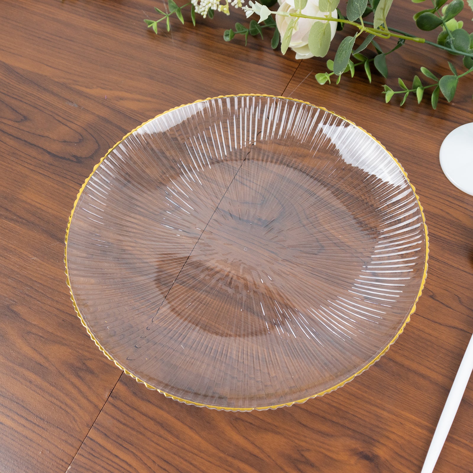 Clear plastic dinner plate with gold rim and ribbed sunburst pattern.