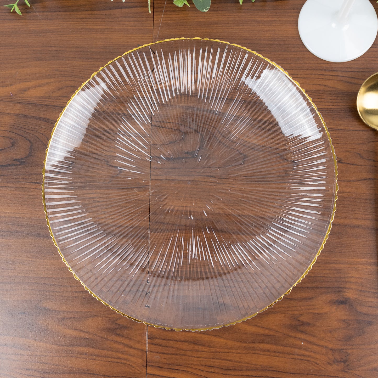 Clear plastic dinner plate with gold rim and ribbed sunburst pattern.