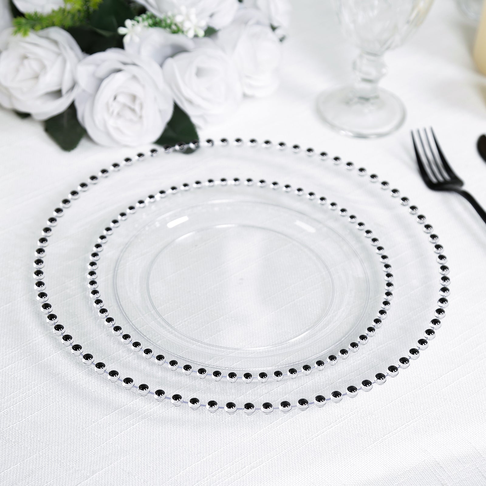 Clear plastic dinner plate with black beaded rim on a white table setting.