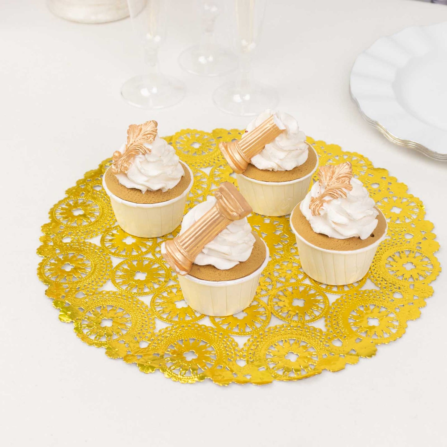Metallic gold paper lace doilies under cupcakes on a table setting.