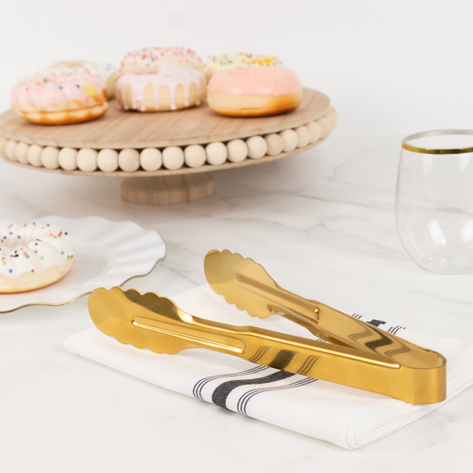 Gold metal kitchen tongs with scalloped edge on marble surface.