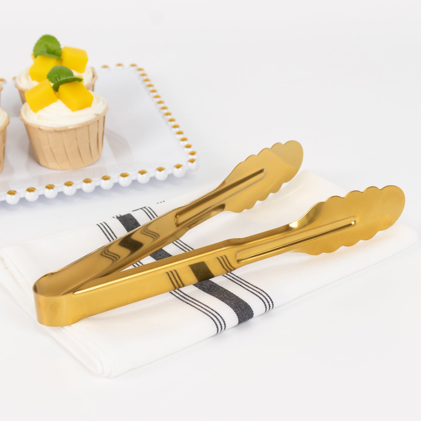 Gold metal kitchen tongs with scalloped edge on a napkin.