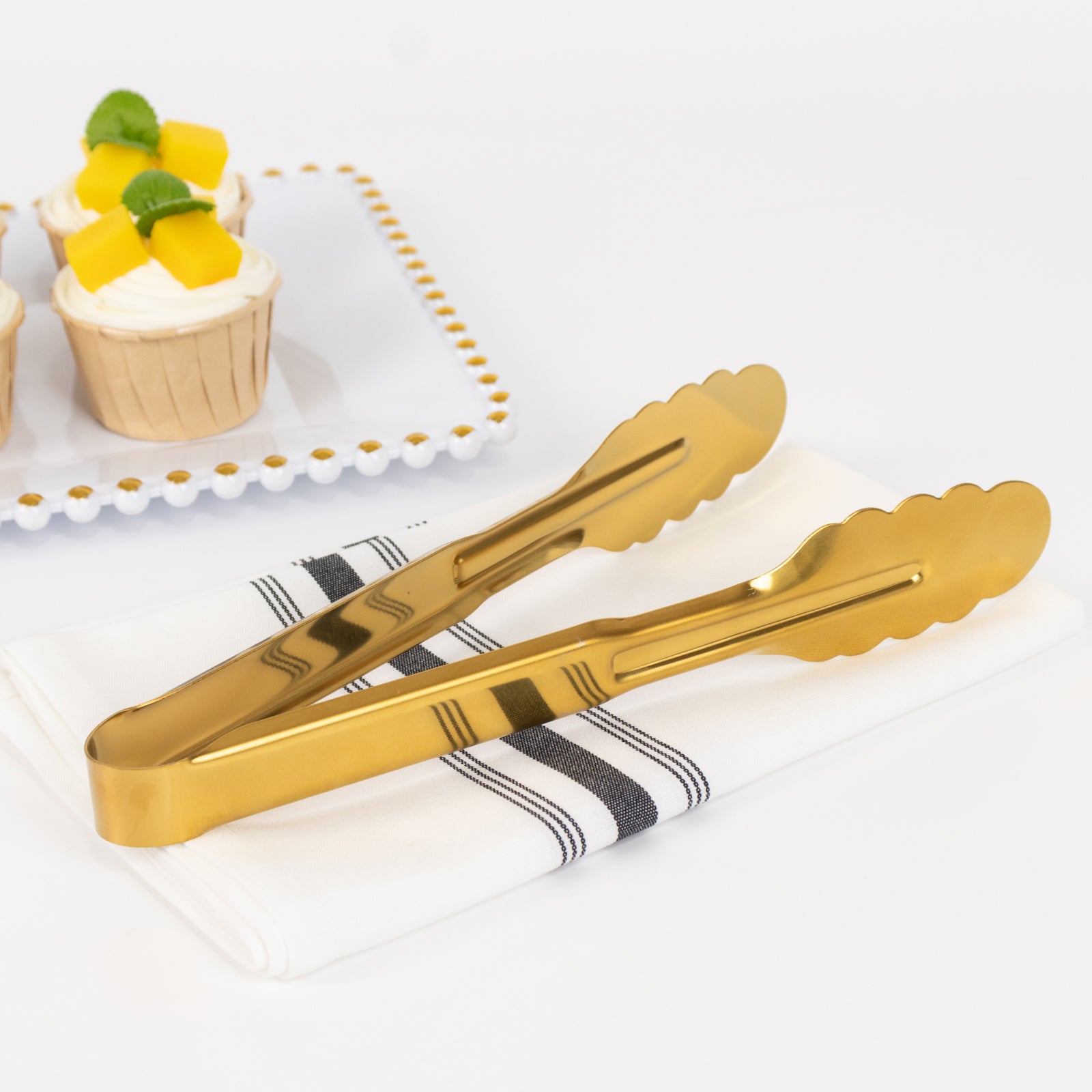 Gold metal kitchen tongs with scalloped edge on a napkin.