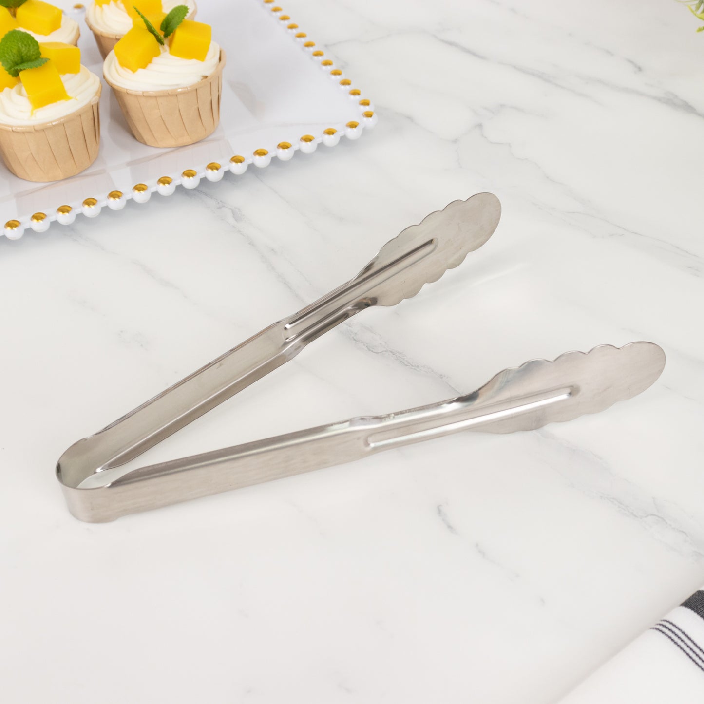 Silver metal kitchen tongs with scalloped edge on marble countertop.