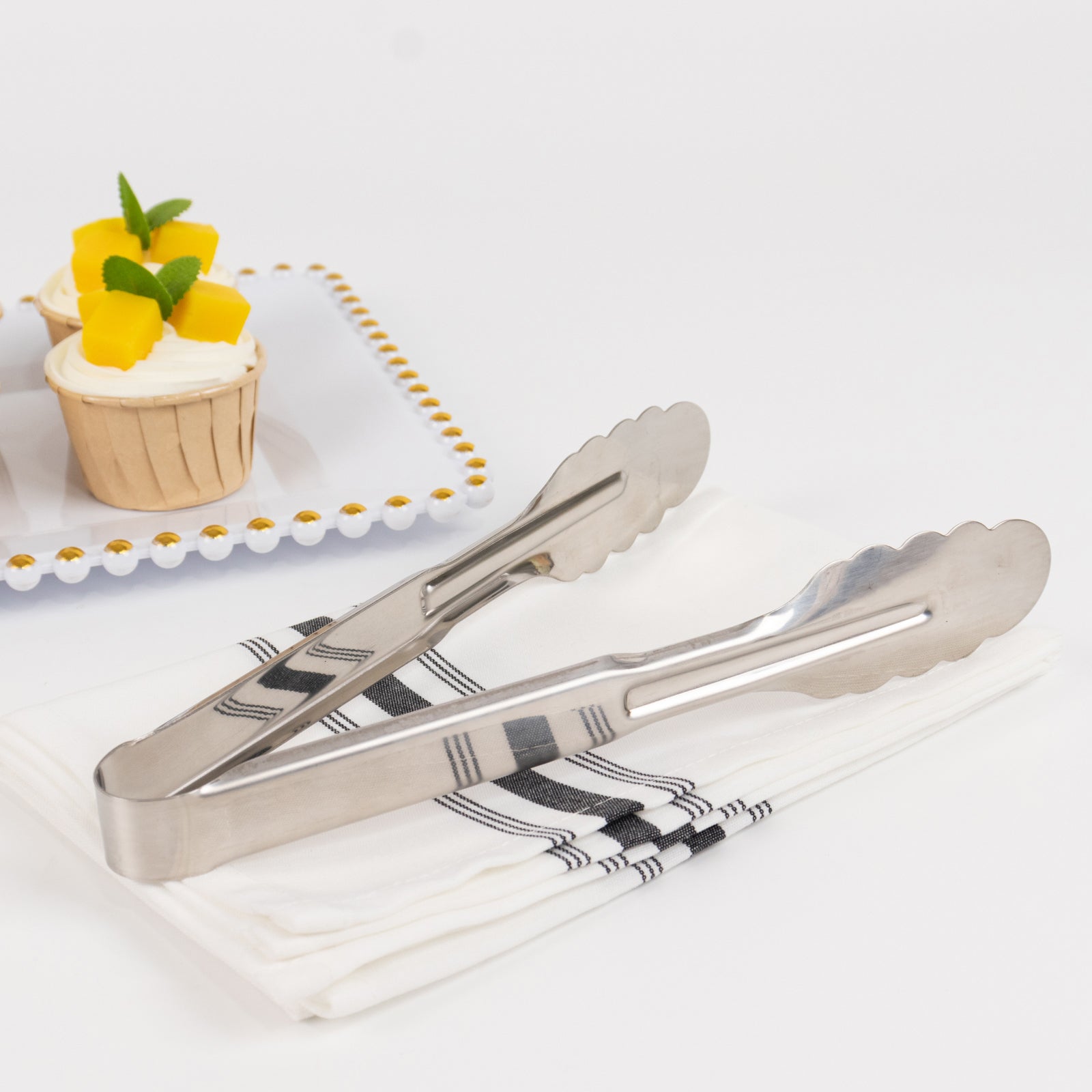 Silver metal kitchen tongs with scalloped edge on a napkin.