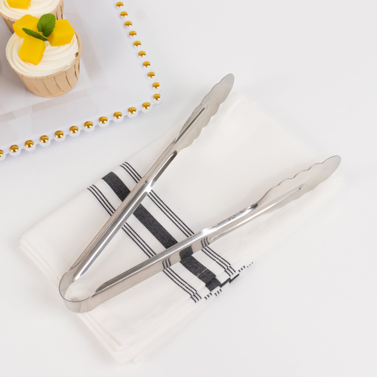 Silver metal kitchen tongs with scalloped edge on a white napkin.
