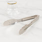 Silver metal kitchen tongs with scalloped edge on a marble surface.