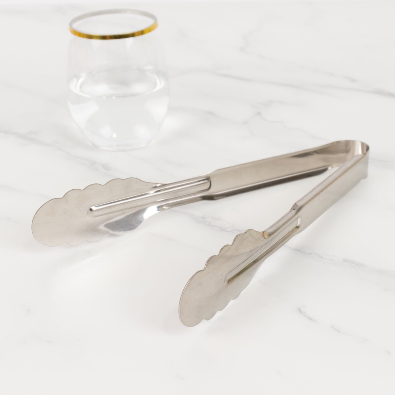 Silver metal kitchen tongs with scalloped edge on a marble surface.