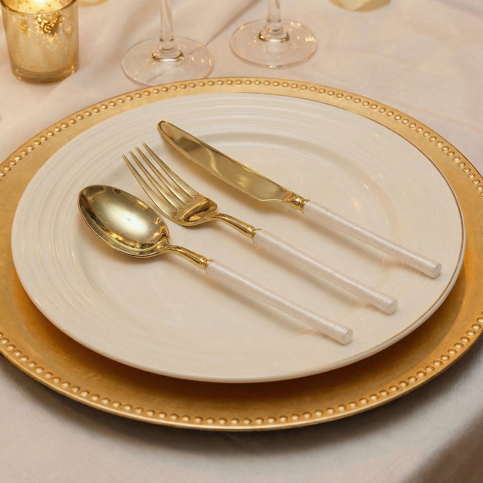 Gold plastic cutlery set with white handles on a decorative plate.#whtbkgd