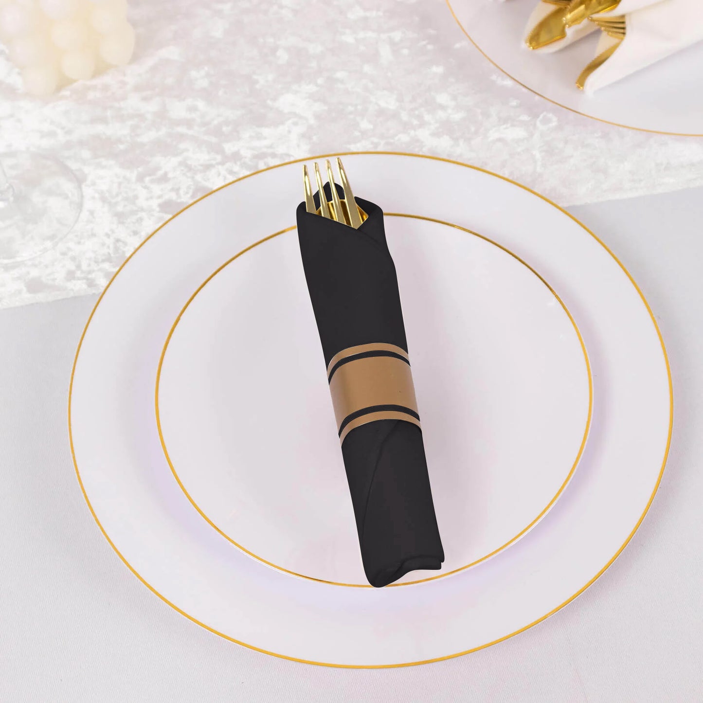 Gold disposable silverware set with black paper napkins on an elegant table setting.