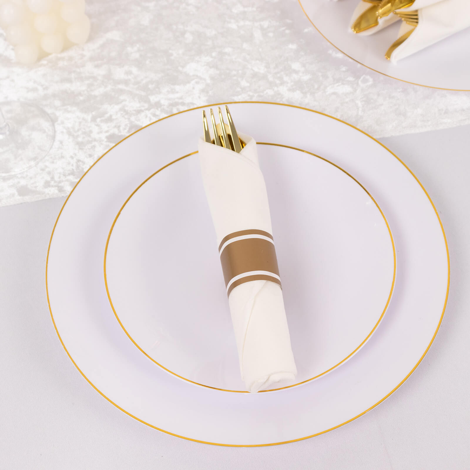 Gold disposable cutlery set with white napkins on a decorative plate.