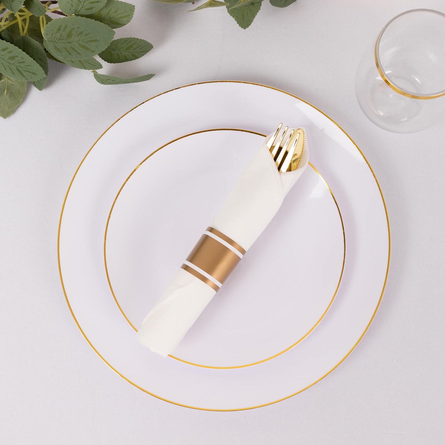 Set of gold disposable silverware with white napkins on a plate.