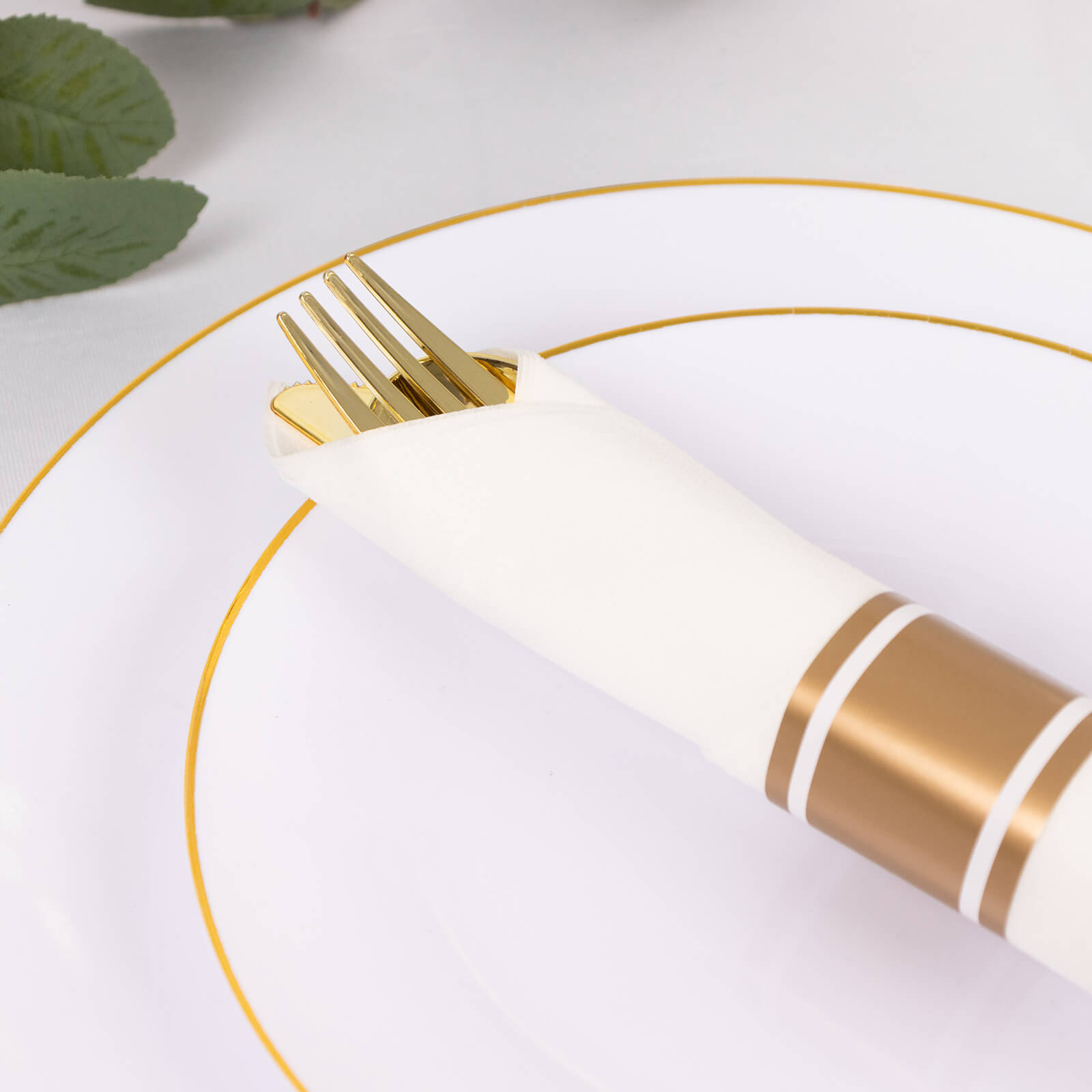Gold disposable cutlery set with white napkins on a decorative plate.