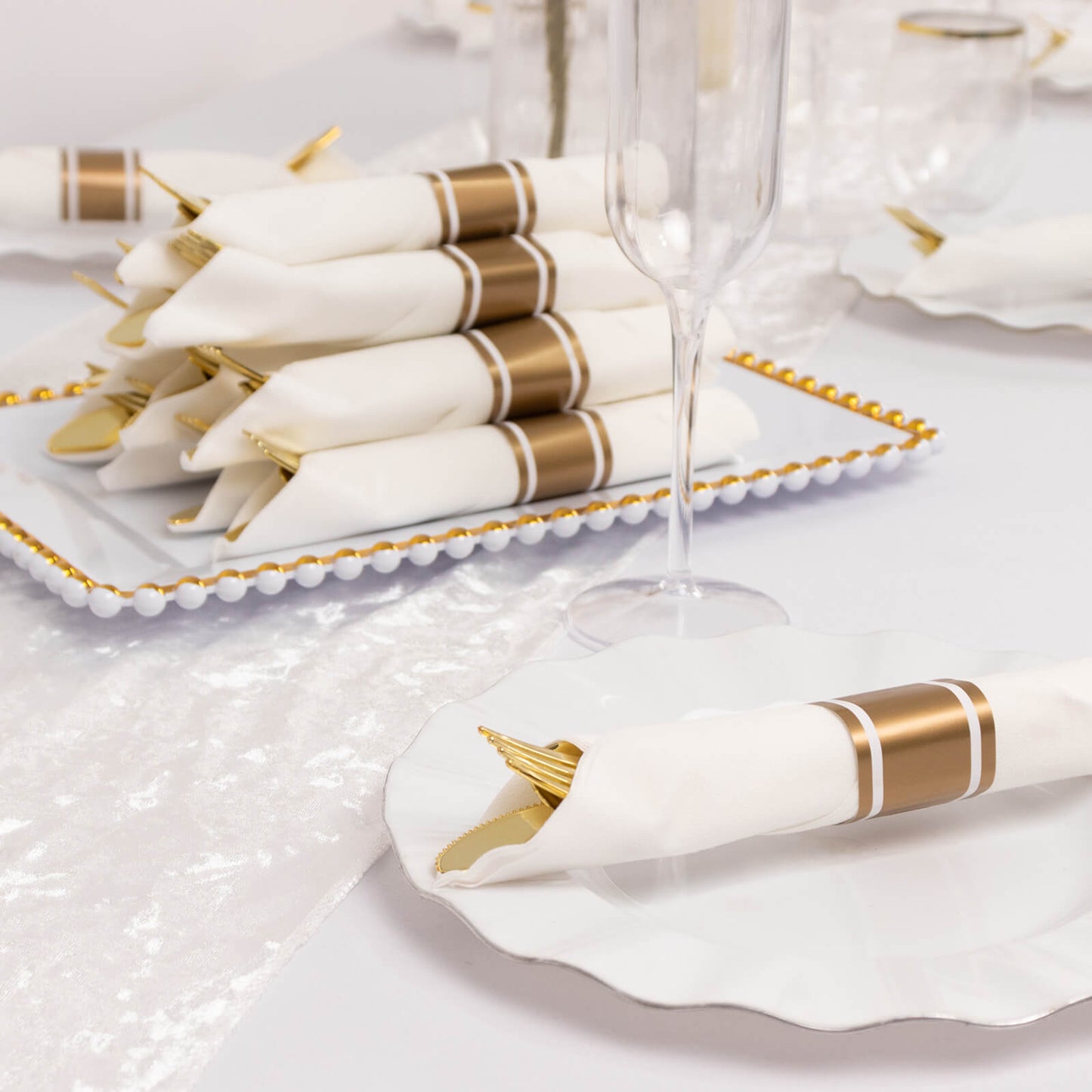 Gold pre-rolled silverware set with white napkins on a decorative platter.