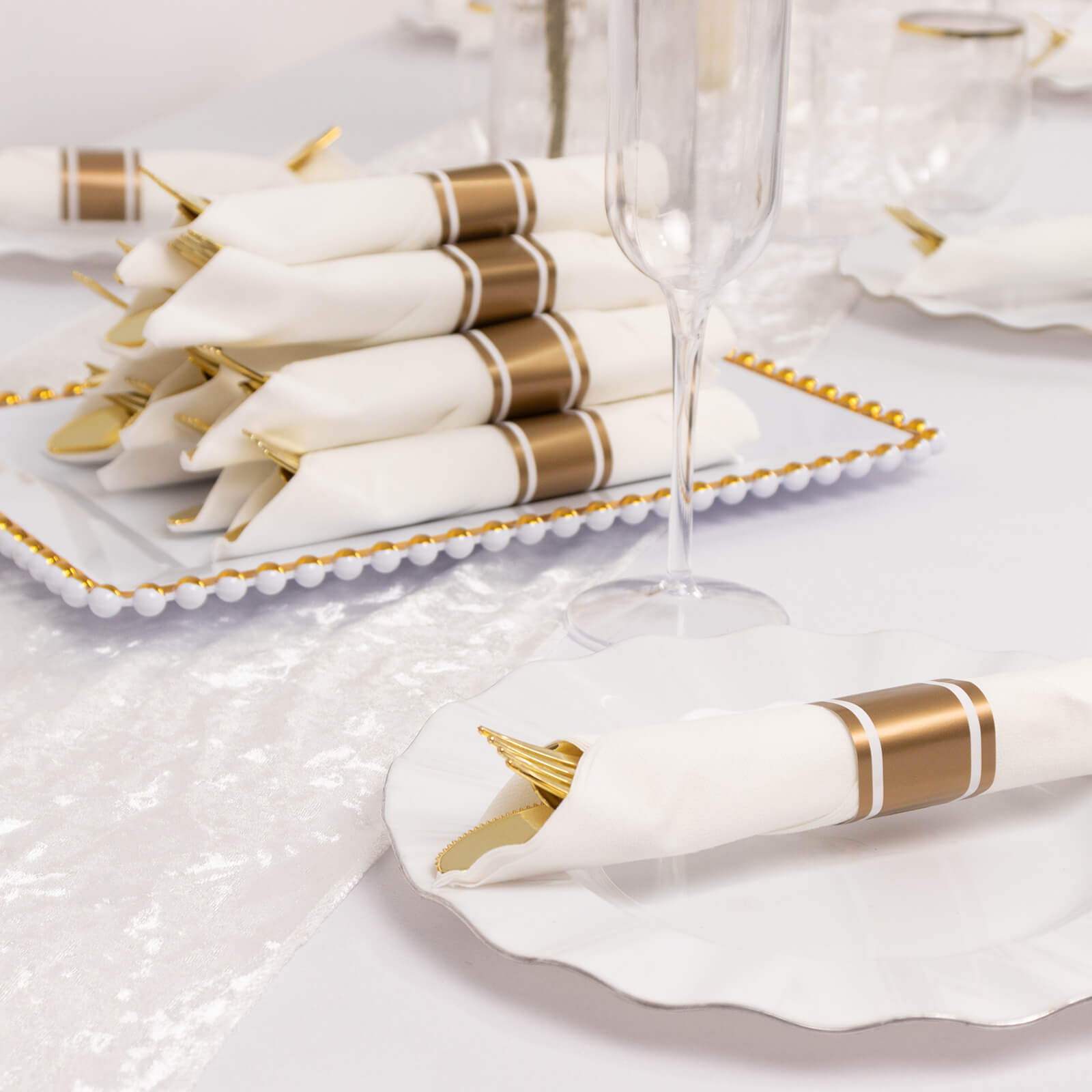 Gold pre-rolled silverware set with white napkins on a decorative platter.