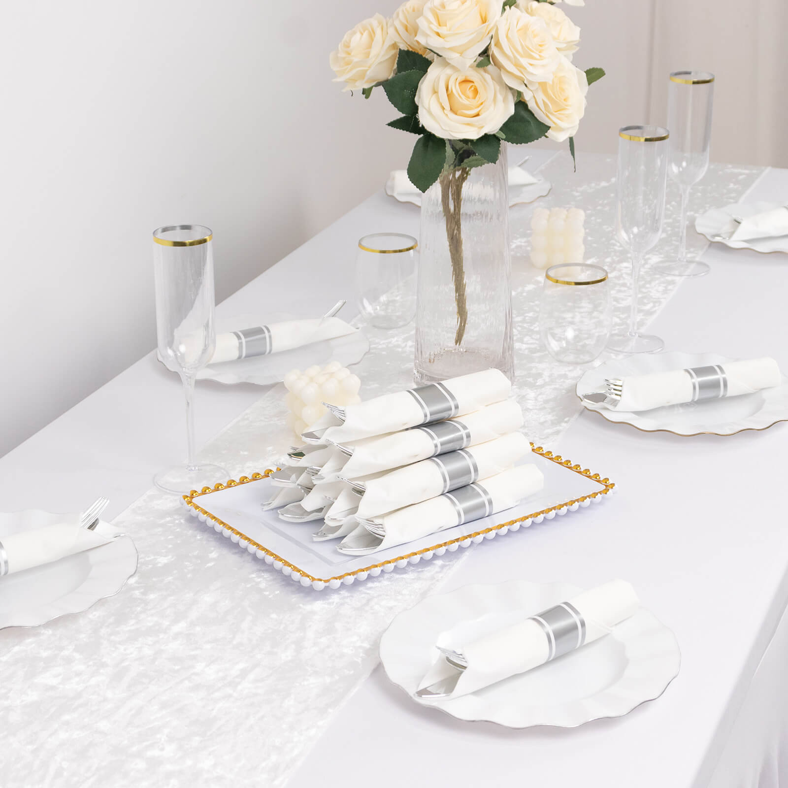 Set of 24 silver disposable cutlery with white napkins on a table.